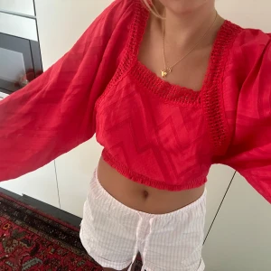 Röd croppad blus - Säljer en snygg röd croppad blus med långa ärmar. Blusen har ett fint mönster och detaljer vid halsen. Perfekt för sommaren eller en festkväll! 💃