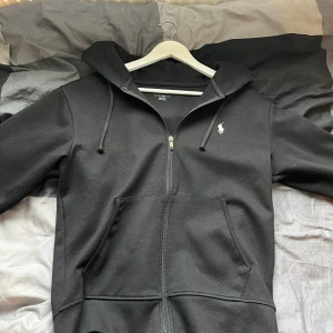 Svart hoodie från Polo Ralph Lauren - Säljer en svart hoodie från Polo Ralph Lauren i storlek S. Den är supermjuk och bekväm, perfekt för höst och vinter. Hoodien har en dragkedja framtill, en praktisk känguruficka och en liten vit logga på bröstet. Den är i nyskick och har knappt använt