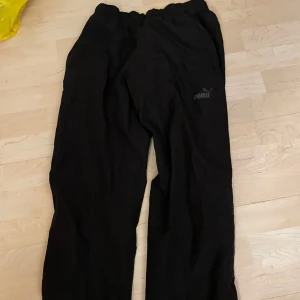 Svarta mjukisbyxor från Puma - Säljer ett par svarta utebyxor från Puma. Byxorna har en elastisk midja och Puma-loggan på ena benet. Perfekta för en avslappnad stil!