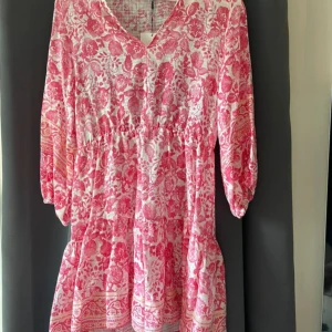 Rosa blommig klänning - Säljer en superfin rosa klänning med blommigt mönster. Klänningen har en v-ringad hals och trekvartsärmar. Den är perfekt för sommarens alla fester och har en lös passform som gör den bekväm att bära. Materialet känns lätt och luftigt, perfekt för varma dagar.