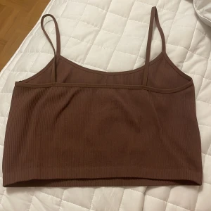 Brun ribbad linnetopp - Säljer en snygg brun ribbad linnetopp. Den är ärmlös med smala axelband och har en tight passform. Perfekt för sommaren eller som ett lager under en tröja. Materialet är mjukt och stretchigt, vilket gör den bekväm att bära hela dagen. Lappen i ryggen saknas. Köparen står för frakten! 