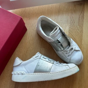 Valentino skor - Valentino Garavani Open Sneakers.  Vita med silver band i storlek 38.  Väl använda, slitningar framtill samt lite missfärgade i blått fram på sulan. Låda samt kvitto medföljer. Köpta för 490£~ 6.670kr i frankrike