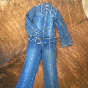 Byxdress jeans  - Jag ÄLSKAR den här, men den passar inte mig längre. Fint skick. Lätt utsvängda ärmar och benslut. Benslut till Axel- 149cm Innerben- 82,5cm Höfter- 39cm Mellan Axelsömmar-34cm Axel till höfter-47cm Bröst-40cm Ärm-58cm