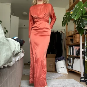Satinklänning - Sofistikerad roströd och långärmad klänning som går ner till golvet på mig som är 165 cm. Bara använd på en bal och kemtvättad efter, köpt på asos för 750kr där den nu är slutsåld!