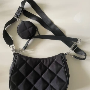 En axelväska - En svart axelväska med en liten väska vid axel bandet med bra skick. Man kan dessutom ta bort det långa bandet så att den blir till en liten axel väska. (Pris kan diskuteras)