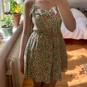 Klänning  - Somrig klänning med volanger. Supergulligt mönster med hallon och blommor. Axelbanden går att justera och man kan knyta i midjan. 🌻