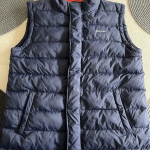 Väst Gant - Marinblå väst från Gant med röda detaljer. Knappt använd. Inget slitage. Täckväst ej dun. 14-15 år. 170 cm.