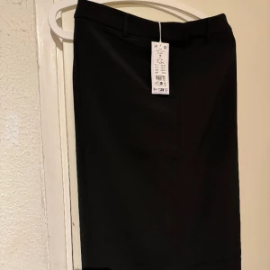 Lång Kostymkjol - Lång kjol i kostymkjol material. Liten slits baktill och stretchigt material. Strl M. Aldrig använd, helt ny med prislapp.