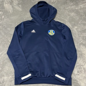 Växjö TS träningshoodie - Överdragshoodie till träning från Adidas. Växjö Tennissällskap. Är för liten för mig och används inte mer tyvärr. I superbra skick men saknar snören till luvan. Storlek M men passar nog även S