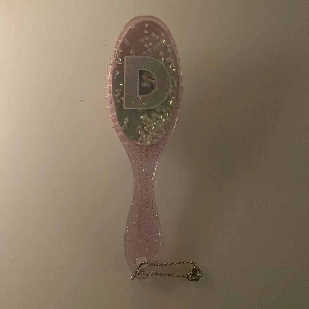 En rosa glittrig hårborste, står även ett D på den, men kan vara användbar ändån❤️liten silver kedja längst ner på borsten, Som gör att du kan hänga det på typ en väska eller något😂. Accessoarer.