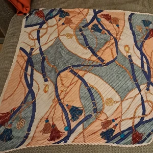 Flerfärgad halsduk med tofsar - En elegant halsduk med ett mönster av rep och tofsar i färgerna blå, grå, beige och röd. Halsduken har en kvadratisk form och är tillverkad i ett mjukt material. kan använda som halsduk eller i huvud eller i vaskan... in many ways!