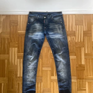 Blå jeans från Dsquared2 - Ett par blå jeans från Dsquared2 i storlek 42. Jeansen har en sliten look med ljusare partier och är tillverkade i Italien. Säljer pga de inte passar mig och gillar inte denna stilen längre. Använda i bra skick