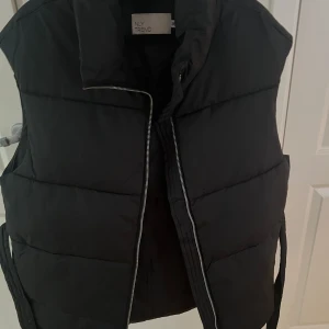 Väst Nelly - Svart väst från nelly med dragkedja som man knyter i midjan, storlek 36 men passar också 38 då man knyter den. Knappt använd, i princip nyskick. Pris 150kr, kan gå mer vid snabb affär.