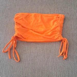 Orange tubtopp - En orange tubtopp med knytband på sidorna. Toppen är ärmlös och har en tight passform.