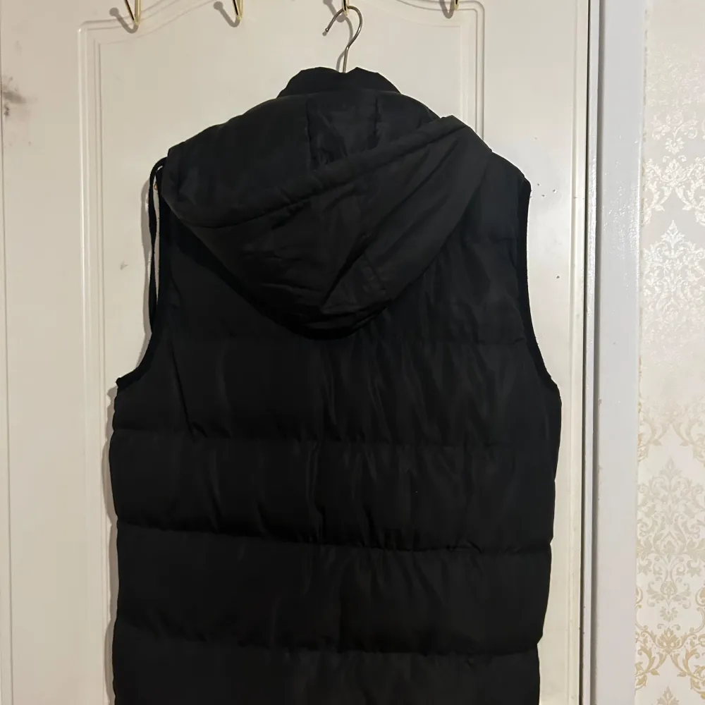 Svart väst med huva. Dragkedja med fickor vid sidorna och snören längs huvan. Puffer väst. Använts Max 5 gånger. Inga synliga fläckar eller märken. Pris kan diskuteras. . Takit.