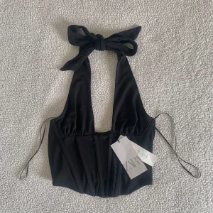 ZARA svart korsett topp med rosett - Supersnygg topp från ZARA i korsettmodell som knyts till rosett i nacken. Ny med tags kvar, utan anmärkningar.