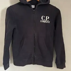 Svart Cp company hoodie i juniorstorlek 10 år. Liten defekt i vänstra ärmen.
