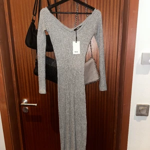 Ribbad grå tygklänning från Bikbok - En lång grå tyg klänning som formar sig efter figuren, med slits på sidan! Väldigt skönt material och helt oanvänd med prislapp kvar!🩶Storlek XS 🩶
