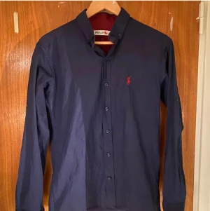 Ralph lauren skjorta - Säljer min Ralph lauren skjorta Slim Fit då jag inte längre har någon användning för den. Den är i storlek M men passar S också. Den är marinblå och man kan vika ner kragen eller vika upp armarna så är det rött inuti.