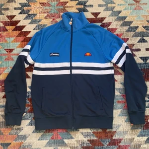Ellesse ziptröja - Jättebra skick, finns inget fel på utsidan. Däremot en väldigt liten fläck på insidan, skicka för bild. Men syns verkligen inte när man har på sig den. St M, men funkar för dig som har S. Nypris 1200kr