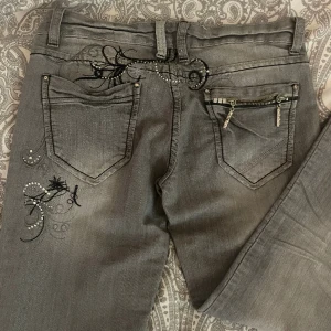 Lågmidjade gråa jeans  - Lågmidjade gråa jeans med super snygga broderingar och stenar på. Köpta på Plick men aldrig använda av mig då dom inte passar. 