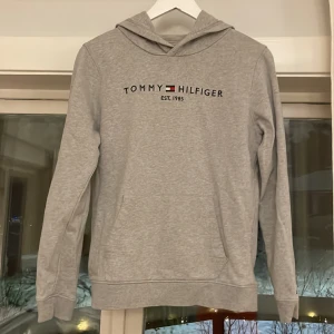 Hoodie - En ljusgrå huvtröja av märket Tommy Hilfiger i strl 164 säljes. Är i gott skick och fläckfri.