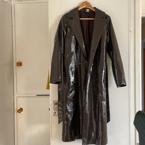 Brun glansig kappa - Kappa från H&M. Kappan är en aning varmare då den är väldigt lätt fodrad.  Inköpt för cirka 1000 kronor, säljes för 450 inklusive frakt.   Nyskick. Bälte i midjan och rymliga fickor!  Kan gå ner i pris vid snabb affär.