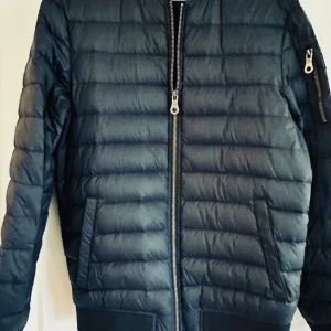 Tunn dunjacka, Lexington  - Fin tunn dunjacka från lexington, marinblå, storlek Small. 2 sidofickor fram på jackan. En innerficka med dragkedja och en med knapp.  En ficka med dragkedja på ärmen.