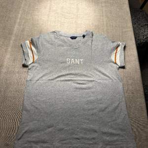 Gant T-shirt Grå med orange vita ränder på armarna. 