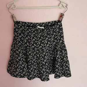 Somrig ribbad kjol. - en kjol perfekt för sommaren. Ribbad svart färgad kjol med vita blommor. Storlek: 160 