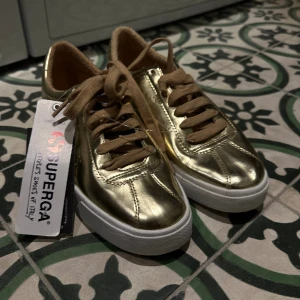 Helt nya guldskor från Superga - Helt nya guldskor från märket Superga i storlek 37. Hör av dig för fler bilder eller övrig information jag glömt skriva/visa. 