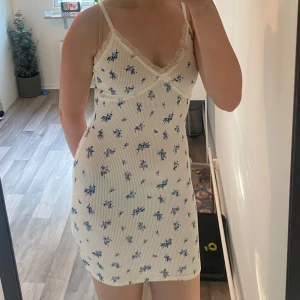 Klänning  - Vit klänning med blåa blommor, spets vid kanten och rosett, bra skick 