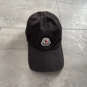 Moncler keps  - En moncler keps som är köpt för ett par år sedan, den är i bra skick eftersom att jag har färgat den för den var solbränd ( qr kod och allt funkar fortfarande) Det tråkiga var att när jag färgade den så fick spännet bak fick lite färg. (Bud pm) 