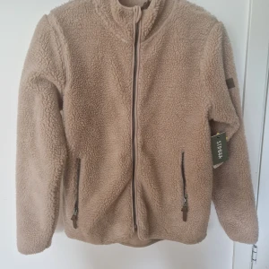 Teddyjacka  - Lapp kvar.  Storlek: S - 36/38 Material: 100% Polyester  Aldrig använd.  Fluffig teddyjacka i beige färg.  Insidan är inte samma material som utsidan,  se bild.  