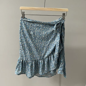 Blommig kjol - Blo kjol med vita blommor på. Från Only i storlek L. Man knyter det översta ”lagret” på framsidan av kjolen i sidan, kan skicka bild om det önskas. Knappt använd.