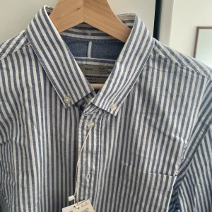 Randig Skjorta i Nyskick - Blåvitrandig skjorta från Mango i stl S som är helt ny, endast testad, bevisas även med prislappen som hänger kvar. 100% bomull. Passar perfekt inför sommaren.