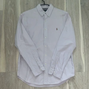 Ralph Lauren Skjorta - En lila Ralph Lauren skjorta i utmärkt skick, som ny. Inga märken eller defekter. Den har inte alls använts mycket. Nypris: 1500 kr. Mitt pris: 500 kr.