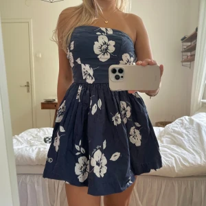 mörkblå bandeau klänning  - såååå söt marinblå bandeauklänning med vita hawaii blommor. den är perfekt till sommaren eller fest! från märket gilly hicks och storlek S, men skulle säga att den passar som en XS. den är tajt runt bysten så att den sitter uppe bra!