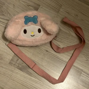 my melody väska - en jättegullig my melody axelremsväska! i ganska bra skick men inte helt ny. ganska använd men inget som syns🫶🏼 jätte bra storlek och man ska iväg och måste ha lite smått med sig! remmen går att justera💕 köpt för 150kr. köparen står för frakten