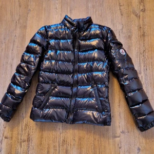 Moncler puffer dunjacka jacka svart lack - Äldre Moncler, cirka 10-12 år gammal. Välanvänd och sliten. Färg: svart. På nära håll syns slitage där lacken börjar släppa, små revor, märken, etc. Size 1 = S 