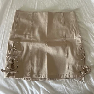 Beige kjol med knytning  - Beige kjol med knytning från bershka. Väldigt stretchigt material, kjolen är aldrig använd och därav i nyskick. Priset kan diskuteras vid snabb affär. Storleken passar S/M.