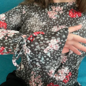 Blommig blus - Blus med volang och en rosett ärmarna.