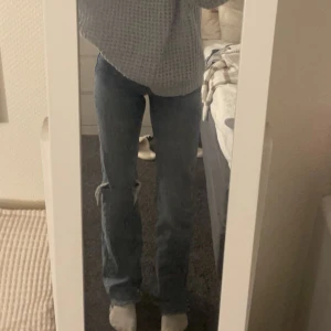 Bootcut jeans - Ett par midwaist bootcutjeans från gina i en blå färg med ett hål på ena benet. Byxorna är långa i benen, passar mig i längden som är 170cm. Längst ner är de ”slitna”, bara avklippta (De ska vara så och var så när jag köpte) De är använda ngr ggr.