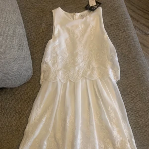 Sommarklänning / Studentklänning - Ny vit klänning från Nelly, fina blommdetaljer, passar till studenten. Storlek 34 men passar 36/38. Aldrig använd, lapparna kvar.