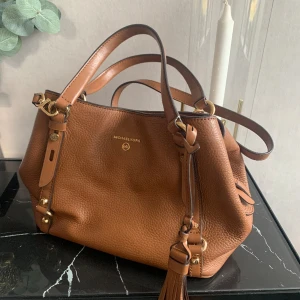 Michael Kors handväska Carrie Tan - Äkta Michael kors handväska Carrie i färgen Tan, fint skick Ca 17 cm hög o 30 cm bred.