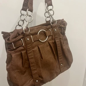 Brun väska - Superfin brun vintage väska som är köpt här på Plick som tyvärr inte kommer till användning. Superbra skick! Får plats med mycket saker för de som brukar ha med sig mycket i väskan!