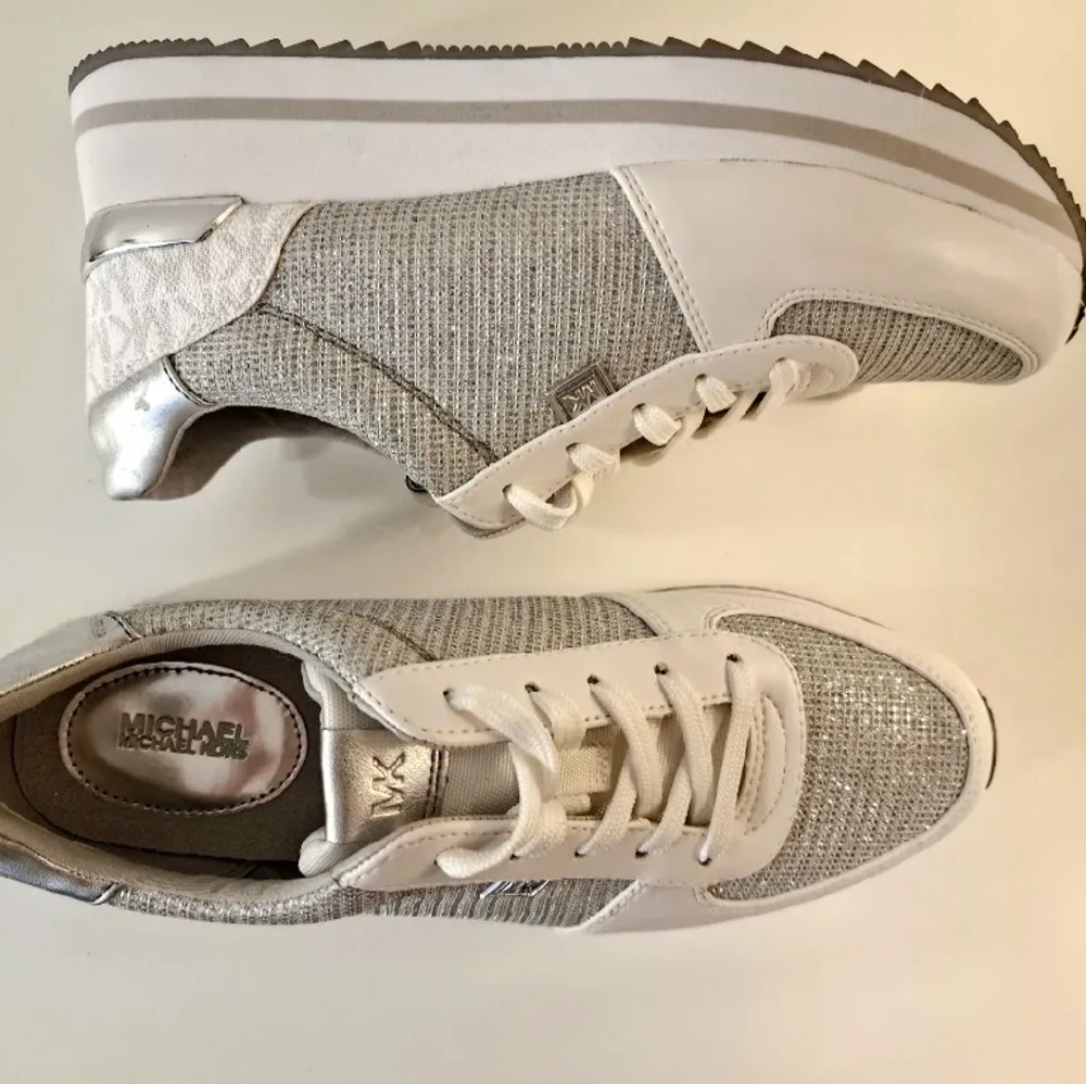 Helt oanvända sneakers i färgerna vit/silver från Mikael Kors. Storlek 38 men passar även en mindre 39. Säljes pga felköp. . Skor.