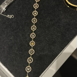 Lily & Rose Armband - Nypris ca 1200:- Sten ramlat Färg  Guld metall o vita stenar. Den stora stenen i mitten av varje blomma är rökt glas (grå)