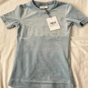 Oanvänd juicy couture velour T-shirt i färgen ljusblå/”Blue Fog”. Storlek XXS. Helt ny med prislappen kvar. Säljs då den aldrig kommit till användning. Säljs inte längre. Nypris: 640kr. Mitt pris: 299kr. Hör gärna av er vid frågor🩵🩵