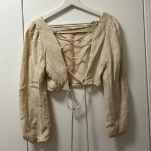 Topp med ballongärm och öppen rygg - Beige croppad topp med ballongärm och knytning i ryggen. Endast använd en gång